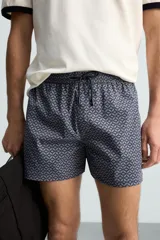 Bañador largo de hombre color rosa pálido con textura seersucker. Presenta cintura elástica ajustable con cordón blanco, bolsillos laterales y un bolsillo trasero de plastrón.