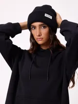 Gorro tipo beanie de punto acanalado color bordó, con etiqueta rectangular blanca con logo de la marca en el frente.