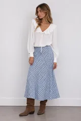 Blusa blanca de manga larga con escote en V y cuello con volados. Cuenta con lazos para atar en el pecho y puños anchos con botones dorados.