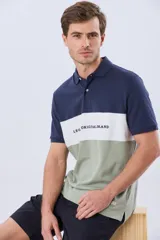 Remera polo de manga corta con diseño en bloques de color en tonos azul marino, blanco y verde militar, con bordado frontal y cierre de botones.