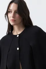Saco tipo capa de punto color negro, con silueta fluida, corte amplio y cierre frontal con dos botones dorados.