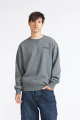 Buzo Quiksilver modelo Lavi de color gris melange, cuello redondo con detalle triangular en el escote y pequeño parche con logo en el pecho.