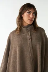 Capa color crudo de tejido de punto 100% lana fina, con cuello alto, cierre frontal con botones, bolsillos delanteros y corte asimétrico.