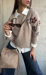 Sweater de punto color beige con cuello redondo y diseño de flores bordadas en tonos oscuros en el frente y las mangas.