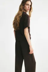 Pantalón sastrero de tiro alto y piernas amplias, color marrón, con pliegues frontales y traseros.