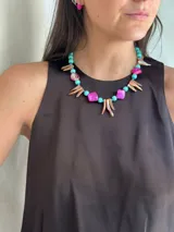 Collar corto con cuentas de nácar teñido en tonos fucsia y turquesa, piedras naturales y mostacillas. Incluye piezas alargadas de nácar iridiscente. Se cierra con cadena de acero quirúrgico.