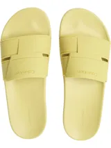 Ojotas tipo slide de Calvin Klein, color amarillo pálido. Presentan una suela moldeada ergonómica con soporte para el arco plantar y una capellada de doble tira de TPU con diseño en relieve y el logotipo de Calvin Klein grabado.
