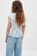 Top de algodón color celeste con estampado floreado, escote corazón y mangas con volados. Presenta detalles de jaretas frontales y corte peplum con vuelo en la parte inferior.