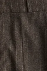 Pantalón sastrero de tiro alto, color marrón oscuro con finas rayas verticales blancas. Presenta cierre frontal con botón oculto y corchetes, bolsillos al bies y bolsillos decorativos traseros. Las piernas son rectas y tienen pliegues marcados al frente y atrás.