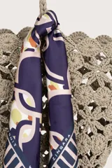 Pañuelo cuadrado con estampado geométrico de cadenas y eslabones entrelazados en tonos morado, crema y dorado, con borde decorativo de líneas y puntos.