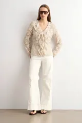 Blusa de encaje beige con escote en V y volados frontales, de manga larga.