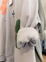 Buzo de cuello redondo en color beige, con diseño oversize y felpa interna. Presenta bordados de flores en tonos rosa, verde y azul distribuidos en el frente.