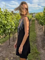 Vestido corto negro de gabardina con corte suelto y escote en V en frente y espalda. La parte delantera está adornada con flecos de lentejuelas plateadas.