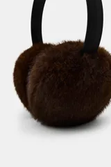Orejeras tipo diadema con estructura de vincha negra y detalle de lazo en la parte superior. Presentan almohadillas con textura de pelo sintético en color marrón.