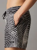 Short de baño negro con estampado de líneas onduladas blancas. Cuenta con cintura elástica ajustable con cordón, bolsillos laterales y trasero, forro de malla y logo de Calvin Klein en el bajo.