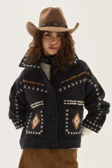 Campera de lana merino hervida en color gris oscuro, con diseño de corte recto, cuello camisero y bolsillos frontales. Presenta bordados artesanales en contraste con motivos geométricos y detalles de costuras en forma de X a lo largo de la prenda.