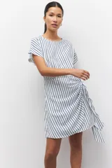 Vestido corto a rayas verticales azules y blancas, de corte suelto y manga corta. Presenta un lazo en uno de sus laterales.