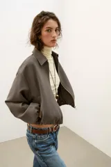 Chaqueta de corte corto y diseño abullonado en color marrón oscuro, con cuello solapa, mangas largas con puños elásticos y cierre frontal con cremallera metálica. Cuenta con bolsillos delanteros de doble vivo.