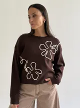 Sweater de punto color marrón chocolate con diseño floral bordado en cordón color crudo. Presenta cuello redondo, mangas largas y puños acanalados.