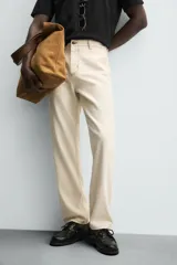 Pantalón de algodón color beige claro, de corte recto (regular fit), con pespuntes en hilo contrastante oscuro. Presenta bolsillos delanteros y bolsillos traseros de parche.