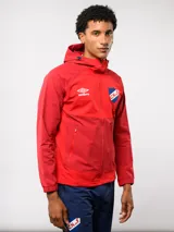Campera deportiva Umbro del Club Nacional de Football, modelo Summit. Presenta un diseño con bloques de color en azul, rojo y blanco, con capucha, cierre frontal y bolsillos laterales con cierre. Incluye el logo de la marca y el escudo del club en el pecho.
