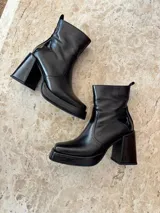 Botas negras de cuero sintético, con caña corta, plataforma y taco cuadrado. Cierre lateral con cremallera.
