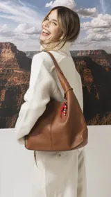 Cartera tipo hobo de cuero sintético color tostado, con diseño de hombro, costuras verticales decorativas y monedero pequeño extraíble a tono.