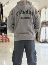 Canguro oversize beige con capucha y cordones ajustables, bolsillo tipo canguro y pequeño bordado en el pecho.