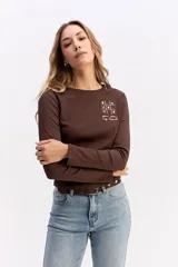 Remera de manga larga color marrón, con cuello redondo y estampa sutil en el pecho con diseño de juego de ta-te-ti y texto.