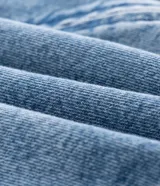 Campera tipo bomber confeccionada en tejido de jean, con cierre frontal de cremallera, capucha ajustable con cordones y bolsillos frontales. Presenta puños y cintura elásticos, ofreciendo un ajuste cómodo y un estilo urbano.