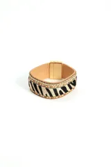Brazalete ancho con base de cuero color beige, estampado de cebra en blanco y negro, bordes con cuentas doradas y cierre magnético dorado.