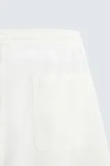 Bermuda de algodón color blanco, de corte relajado (relaxed fit), con cintura elástica ajustable mediante cordón. Posee bolsillos laterales y un bolsillo trasero de plastrón. Presenta un bordado en contraste en la pernera.
