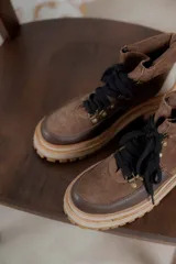 Botas acordonadas de caña baja con diseño combinado en gamuza marrón, cuero marrón oscuro en la puntera y detalle en cuero beige en el talón. Presenta suela track robusta en tono crema y cordones negros.