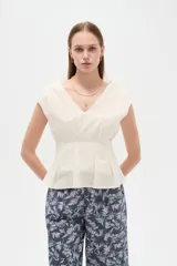 Blusa de lino color blanco, con cuello en V, pinzas de entalle y diseño al cuerpo con faldón acampanado.