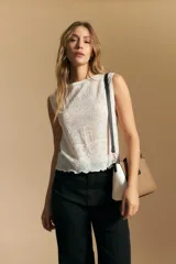 Top sin mangas de jacquard color negro, con cuello cerrado y silueta recta. Presenta una textura trabajada con relieve y una terminación suavemente ondulada en el ruedo.