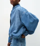 Campera bomber de jean azul con cuello redondo, mangas abullonadas con puños elásticos, cintura ajustable y cierre frontal con botones a presión.