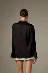 Blusa negra de poliéster, con cuello camisero, mangas largas y cierre frontal mediante tiras para anudar.
