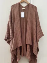 Ruana tejida en punto jersey, color negro con destellos brillantes de lurex. Presenta una etiqueta de cuero sintético con logo en la parte posterior.