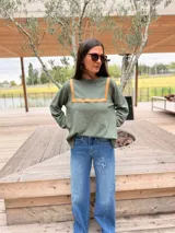 Sweater de tejido de punto color verde oliva, con cuello redondo y detalle de recortes en cuero color camel en la parte frontal. Presenta mangas largas y un corte holgado.