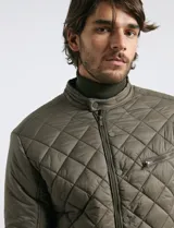 Campera capitoneada de color azul oscuro, con cierre frontal de metal y botones a presión. Presenta bolsillos laterales y en el pecho con cierres metálicos.