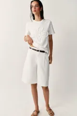 Camiseta blanca de algodón con cuello redondo, manga corta y detalle de flor en relieve bordada en el mismo tono.