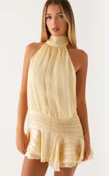 Vestido corto de satén color crema con diseño de rayas verticales sutiles. Presenta cuello alto tipo halter, cintura elástica fruncida y falda con volados en el ruedo.