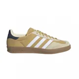 Championes adidas Gazelle Indoor, confeccionados en gamuza color tostado con las icónicas tres tiras laterales en blanco. Presentan suela de goma color marrón, detalle de talón en azul oscuro y el nombre del modelo en dorado.