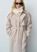 Trench coat de corte oversize en color beige, con cuello de solapa, cierre frontal, cinturón ajustable a la cintura, trabillas en hombros y puños con detalle de botón.