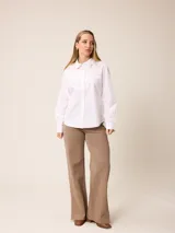 Camisa de corte clásico y calce entallado, color blanco, con cuello camisero, cierre frontal de botones y mangas largas con puños abotonados. Presenta un pequeño bordado distintivo en el pecho.