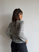 Remera básica de manga larga y cuello redondo, confeccionada en tejido melange en tonos grises y blancos con sutiles destellos multicolores. Presenta un corte recto con aberturas laterales en el dobladillo.