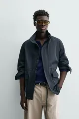 Parka de corte relajado confeccionada en tejido de algodón con efecto lavado. Presenta cuello subido, manga larga con puños abotonados, bolsillos frontales de plastrón con solapa y cintura ajustable mediante cordón interior. El cierre frontal es de cremallera oculta por una solapa con botones a presión.