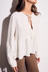 Blusa color crudo de viscosa y lino con bordados en el frente, escote con lazo y mangas largas. Corte holgado con frunce en la cintura.