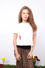 Remera blanca de corte oversize con cuello redondo y manga corta. Presenta un detalle de parche rectangular en color rojo en la parte inferior derecha.