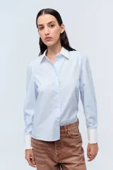 Camisa celeste a rayas con cuello clásico y puños blancos con volados.